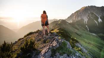 Wandelaar met rugzak staat op een bergkam in Liechtenstein en kijkt in de opkomende zon
