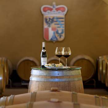 Sfeervolle wijnproeverij in de wijnkelder van de Princely Winery met twee glazen en een fles rode wijn op een houten vat.