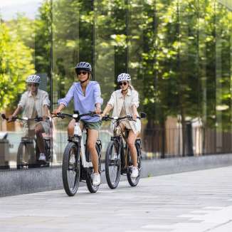 Twee vrouwen op e-bikes rijden door het moderne centrum van Vaduz in Liechtenstein, met zijn glazen gevel en stedelijke flair