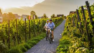 Twee fietsers in de wijngaarden van Liechtenstein bij zonsondergang - e-biketocht met uitzicht op de Alpen en wijnranken