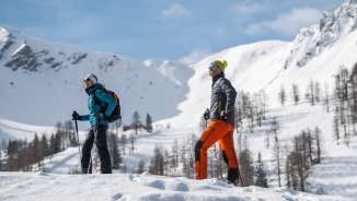 Twee mensen winterwandelen door het besneeuwde landschap van Malbun met besneeuwde bergen op de achtergrond