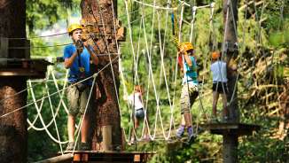 Kinderen en jongeren met helmen op het hoge touwenparcours in het Triesen touwpark in Liechtenstein, gezekerd op klimelementen in het bos