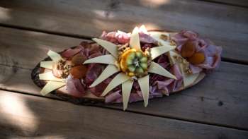 Een artistiek gerangschikt houten bord met verschillende soorten worst, kaas en decoratie van eetbare bloemen, geserveerd op een houten tafel. Een artistiek gerangschikt houten bord met verschillende soorten worst, kaas en decoratie van eetbare bloemen, geserveerd op een houten tafel.