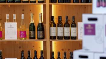 Interieur van de Hofkellerei met stijlvol verlichte houten planken vol wijnflessen en dozen.