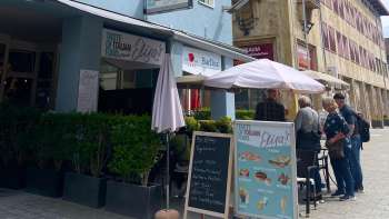 Buitenkant van restaurant Elisas met parasols en een menukaart op een bord