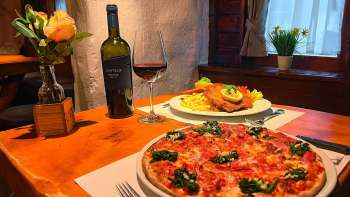Close-up van een pizza met tomaten, kaas en basilicum op een houten tafel, een glas rode wijn op de achtergrond
