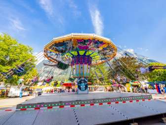 Grote kleurrijke kettingcarrousel op de kermis in Balzers, vol gelukkige bezoekers voor een bergdecor onder een blauwe hemel.