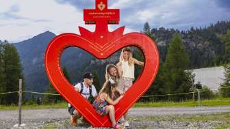 Familie op pad van het Alpijns hart in Malbun in Liechtenstein Familie poseert bij het rode hart frame langs de pad van het Alpijns hart in Malbun, Liechtenstein, omgeven door alpine natuur en bergen.