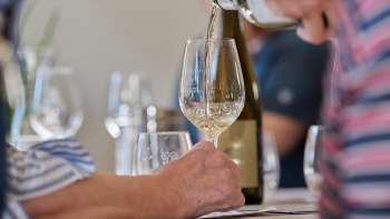 Een glas witte wijn wordt ingeschonken tijdens een begeleide proeverij.