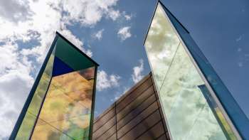 Kunstinstallatie "Two Light Prisms" van Heinz Mack met kleurrijke glinsterende glazen oppervlakken tegen een blauwe lucht.