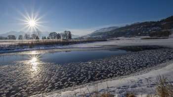 Zonsopgang bij het Egelmeer in Mauren in de winter met glinsterend ijs, sneeuw en een zonnige bergachtergrond.