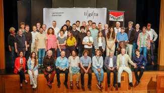 Groepsfoto van de deelnemers en instructeurs van de Liechtenstein Guitar Days (LiGiTa) op een podium voor een spandoek met het logo van het evenement