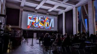 Bezoekers van het filmfestival Schaan 2023 zitten voor het scherm in een moderne avondsetting in Liechtenstein