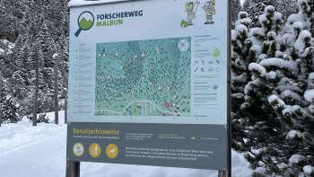 Meisje met groene hoed kijkt door een telescoop op het Forscherpad Malbun met een panoramisch uitzicht op de Liechtensteinse Alpen.