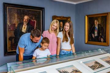 Een gezin bekijkt tentoonstellingen in het Liechtenstein Nationaal Museum in Vaduz, omringd door historische schilderijen en portretten.