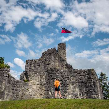 Wandelaar staat met een vlag voor de imposante burchtruïnes Schellenberg onder een blauwe hemel.
