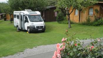 Camperplaats op camping Mittagsspitze met groene weide en omringende houten hutten.