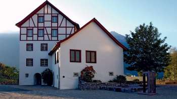 Historisch gebouwenensemble van de Pfrundbauten met vakwerkgevel en bergachtergrond in Liechtenstein in het avondlicht.