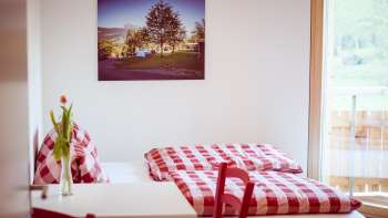 Gezellige tweepersoonskamer in het pension op Camping Mittagsspitze met rood en wit geruit beddengoed en decoratie.