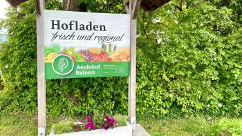 Bord van boerderijwinkel Aeulehof met de woorden "Vers en regionaal" voor een groene haag in Triesen.