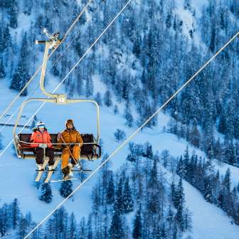 Tina Weirather en Marco Büchel zitten samen op een stoeltjeslift, omringd door besneeuwde bomen en een winters landschap in Malbun.